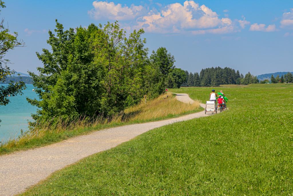 Várias pessoas pedalando de bicicleta em um campo verde na beira de um lago em Fussen