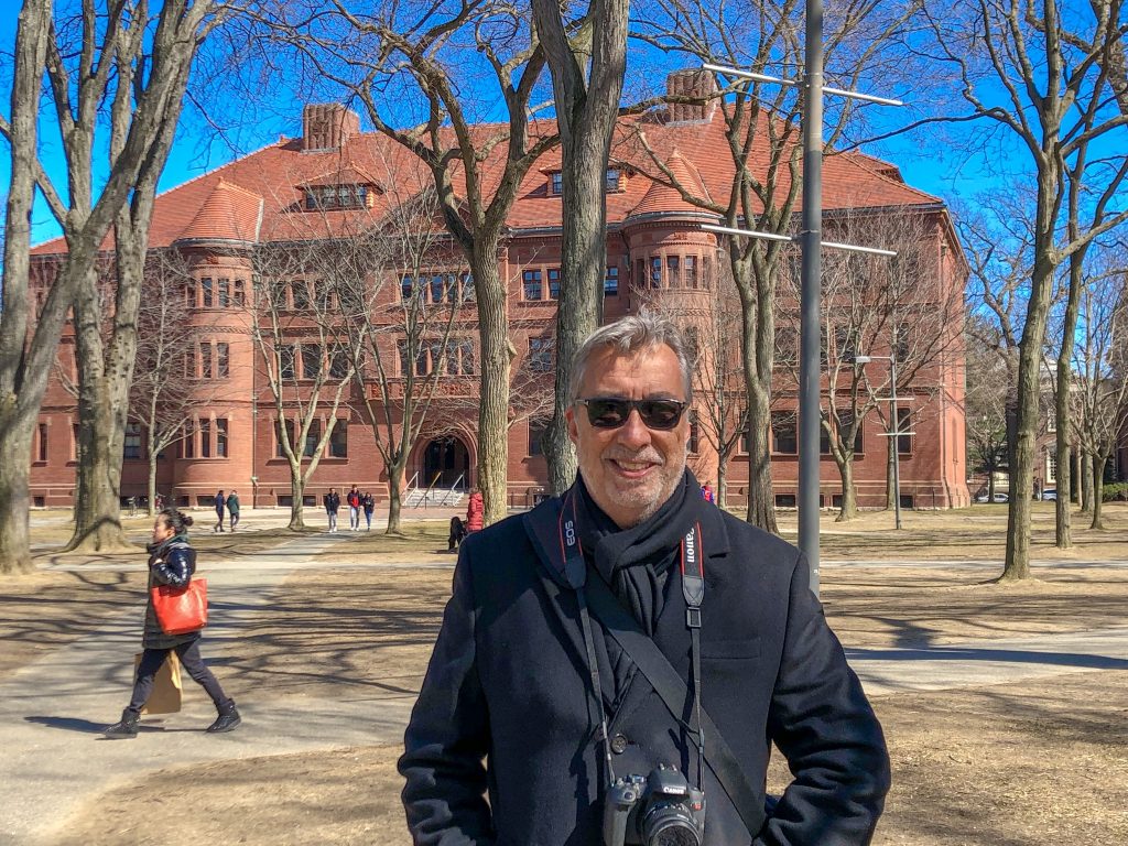 Homem com máquina fotográfica em frente a prédio em Cambridge
