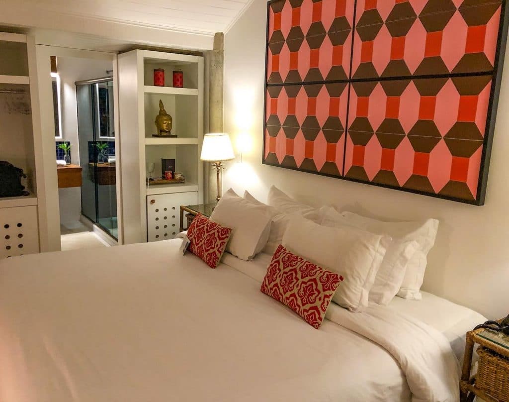 Quarto com colcha branca e quadros coloridos do hotel de luxo em Búzios