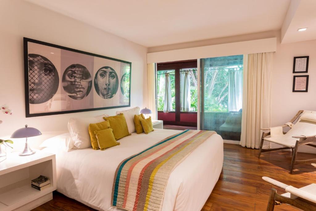 Quarto com cama grande, lençol branco e algumas almofadas, além de poltronas e mesinha de cabeceira de hotel de luxo em Búzios