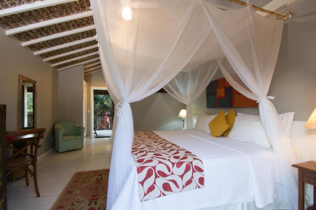Quarto de hotel de luxo em Búzios com colcha branca e poltrona.